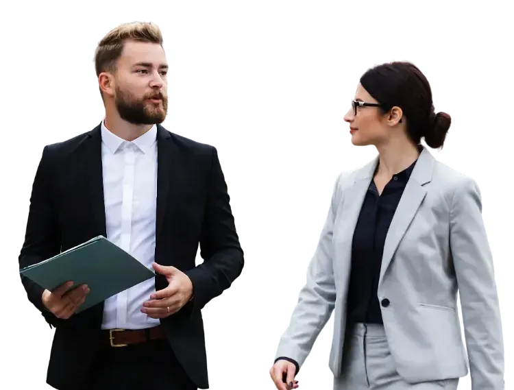 A man in a dark suit holding a folder and a woman in a grey suit walk while conversing against a white background.