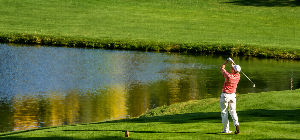 Golfer in red shirt swings near a pond on a lush green course in Front range area of Colorado