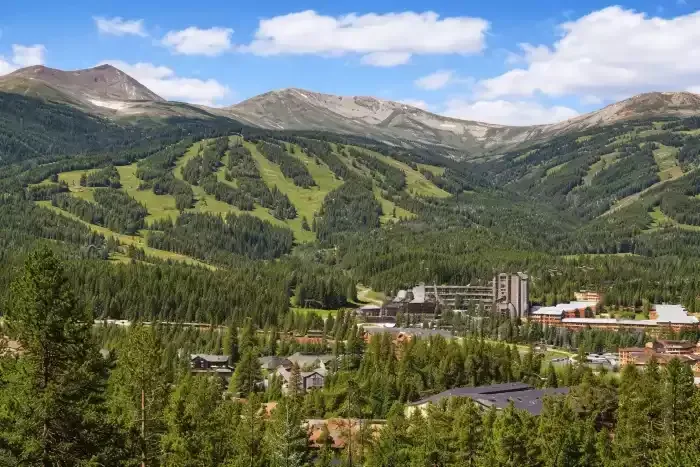 Mountain resort village below green ski slopes and rocky peaks under a blue sky