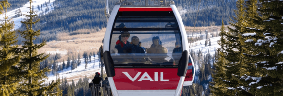 Red Vail gondola with passengers over snowy mountains and pine trees