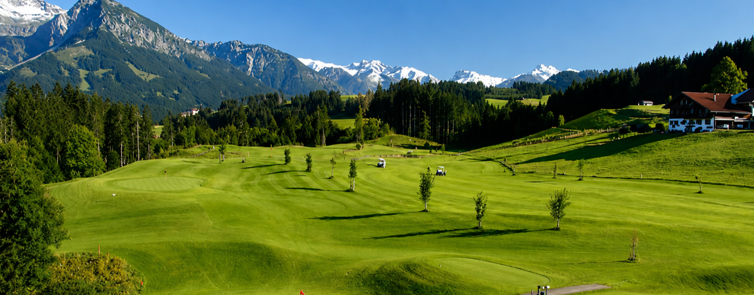 Green alpine meadow with distant mountains, pine trees, and a small cabin under a blue sky in Vail Valley, CO.