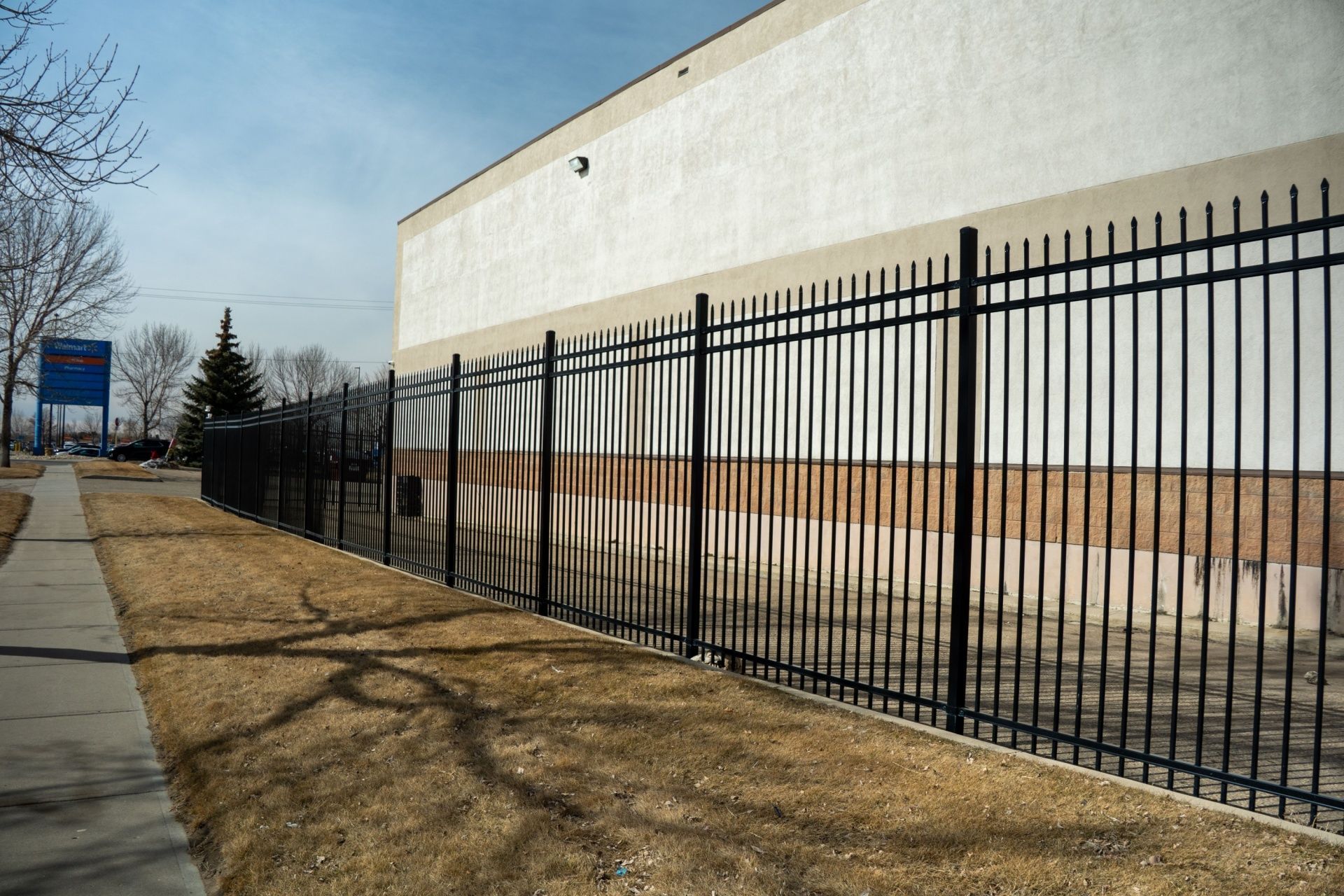 Black metal fence along a building's side, next to a sidewalk and brown grass.