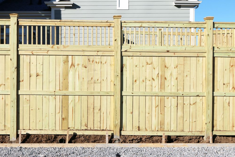 Wooden fence, light brown, with vertical boards and decorative top section, set against a blue sky.
