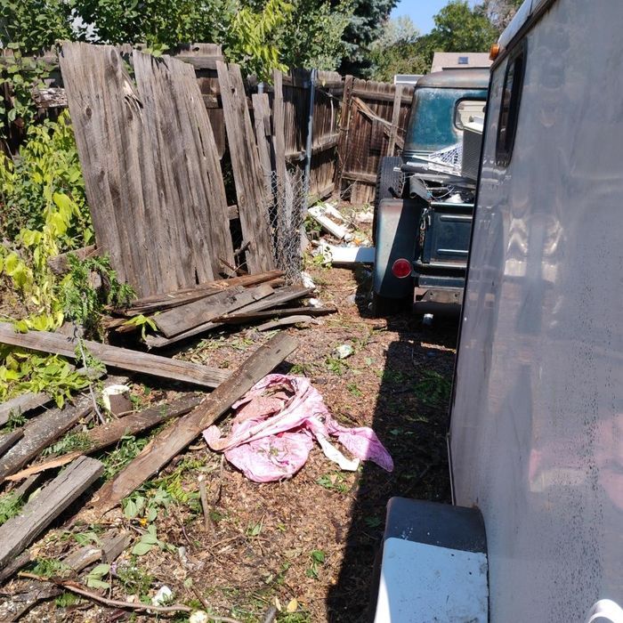 A broken wooden fence with debris next to a parked vehicle and a trailer. Pink cloth on the ground.