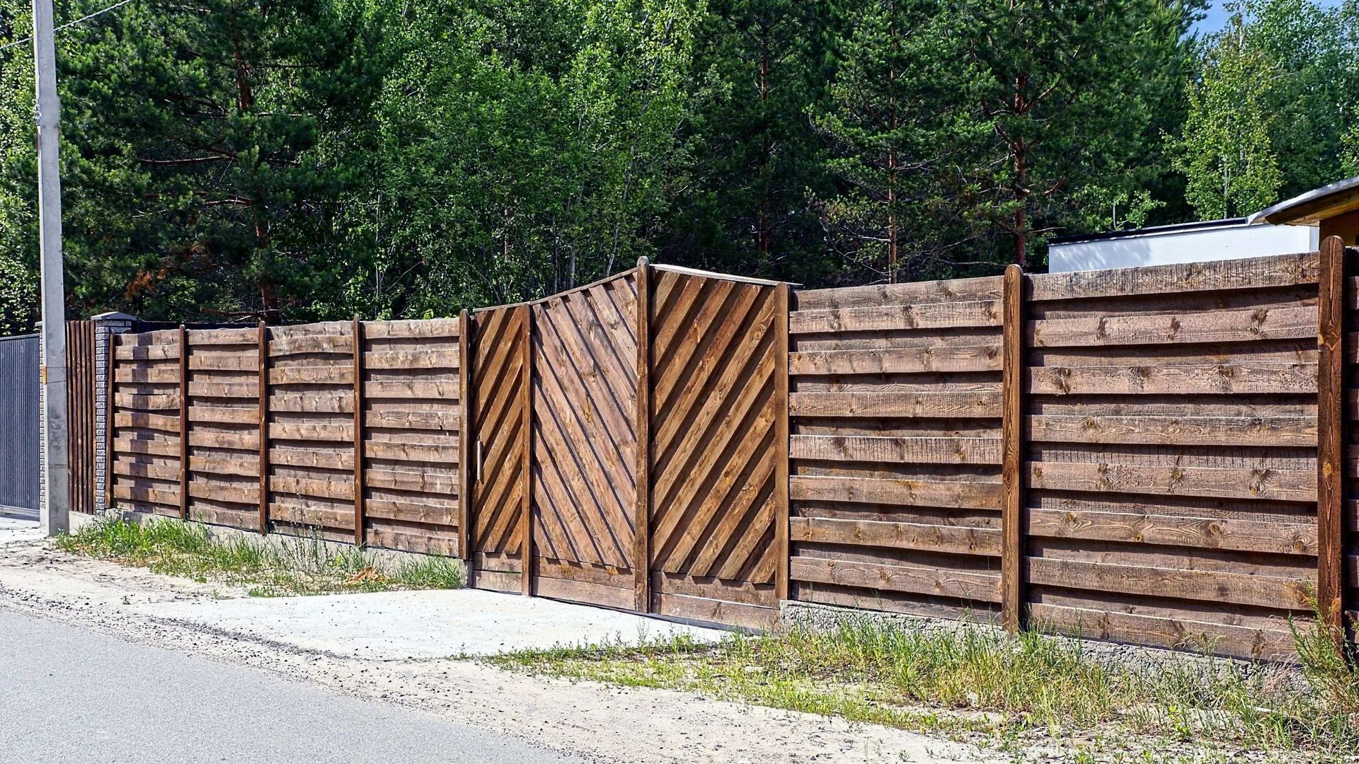 Wooden fence with a gate, next to a road, and green trees.