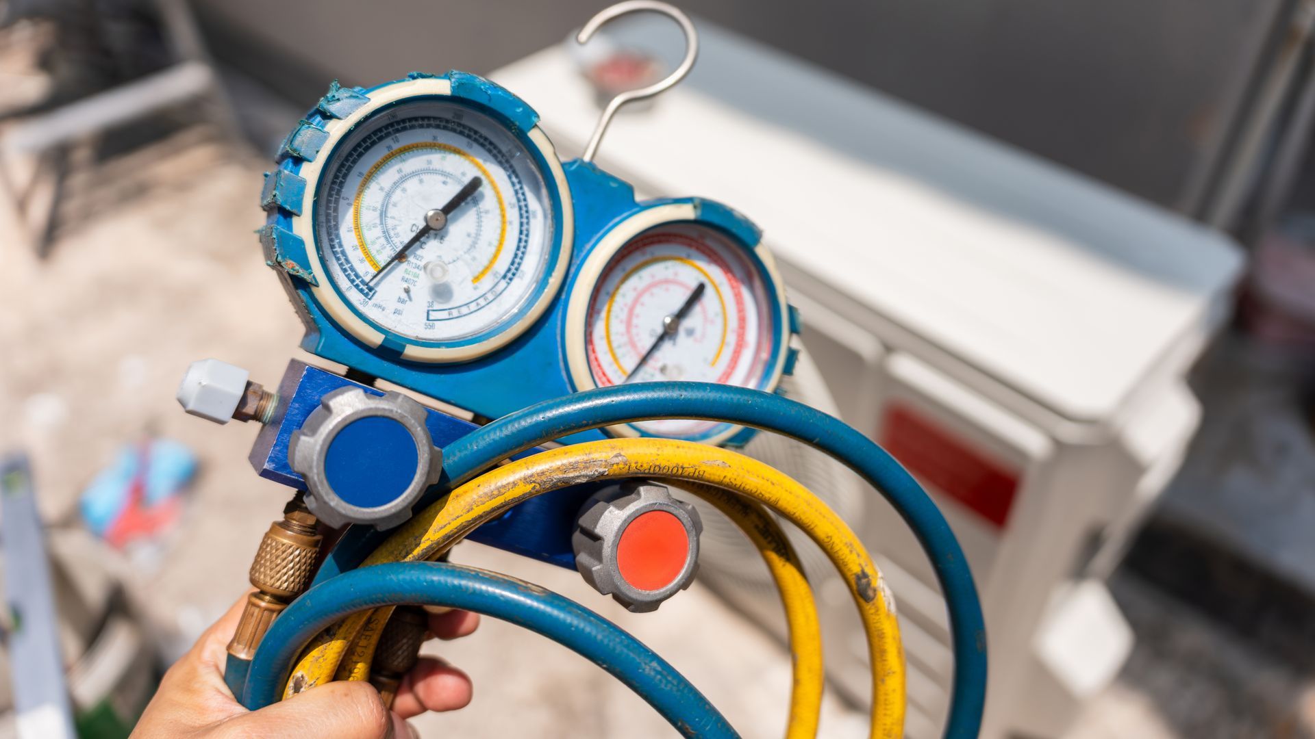Colorful industrial pressure gauges with hoses and a hand adjusting a valve.