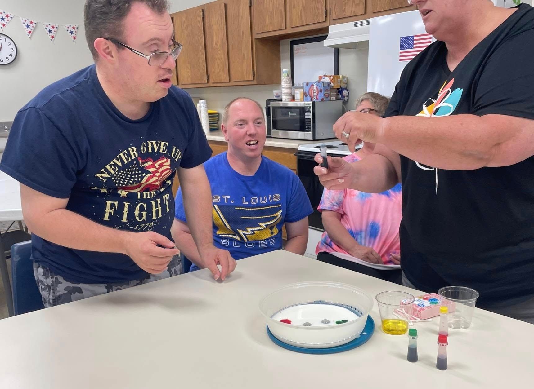 People at a table doing a science experiment, with food coloring and small candies in a bowl.