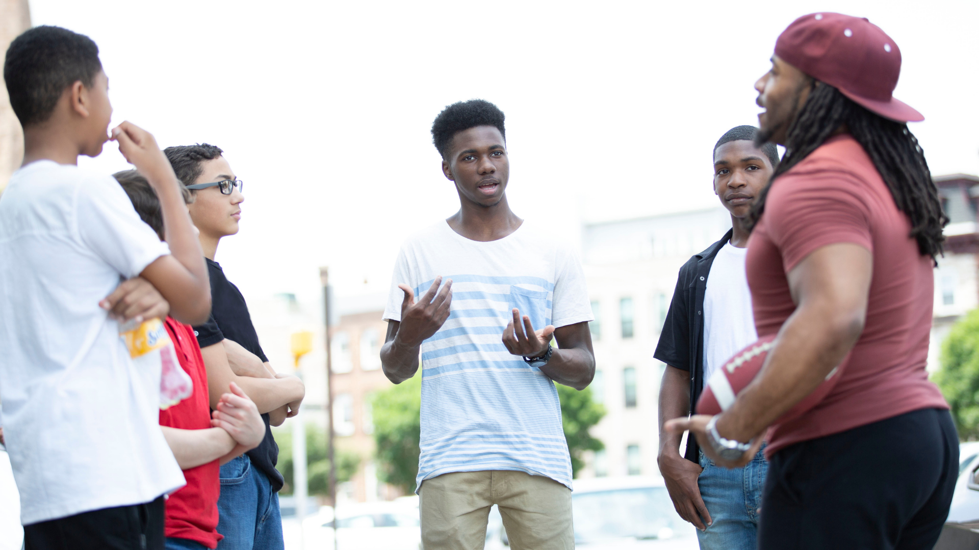 Group of people chatting outdoors, with one man gesturing while others listen.