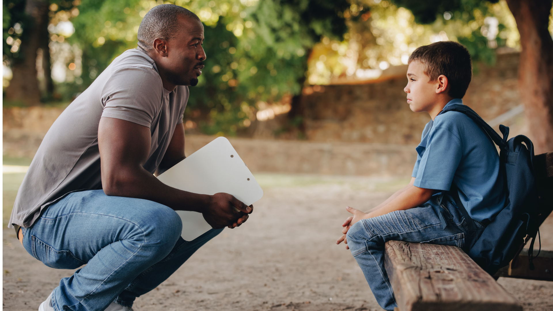 Adult speaking with a child seated on a bench outdoors, in a calm conversation.