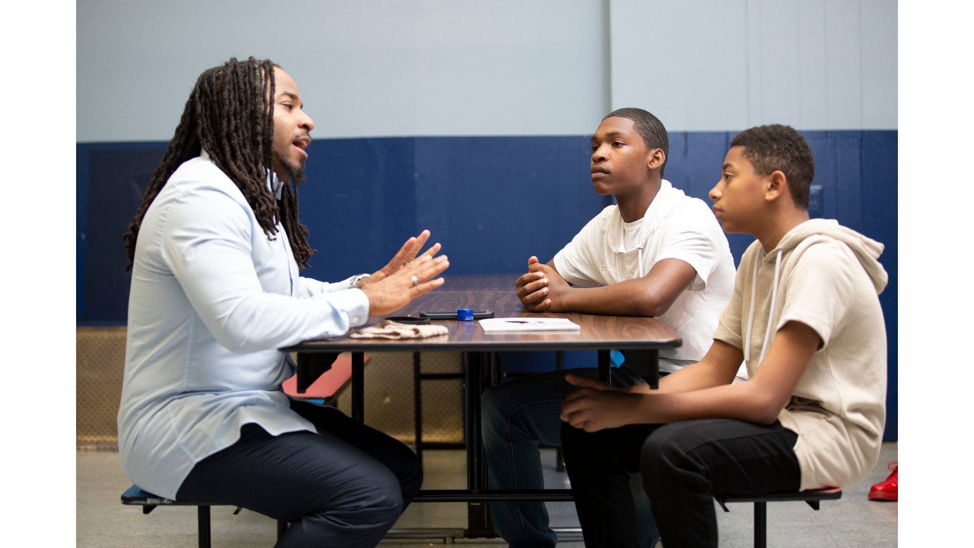 Three people talking at a table in a room, with one woman gesturing as they meet.