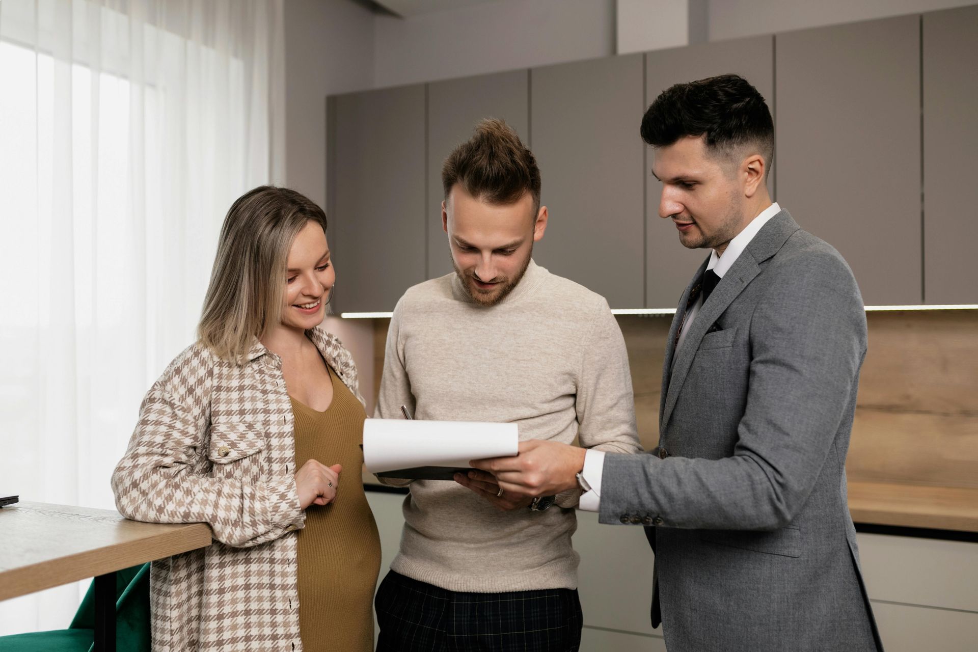 Real estate agent showing document to a couple in a modern kitchen.