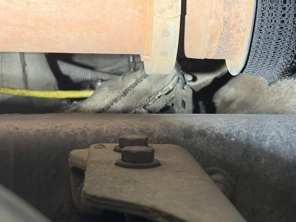 Close-up of a dirty mechanical wheel and bracket with a bolt and yellow hose underneath.