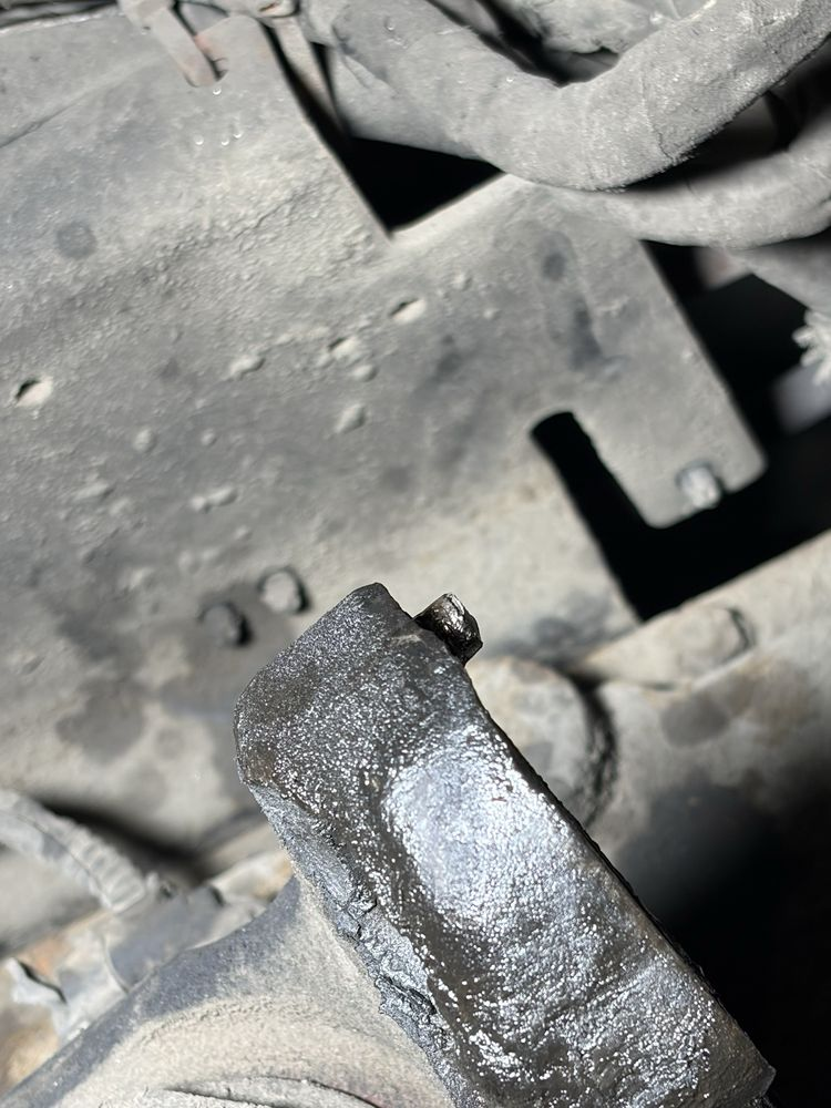 Close-up of a dirty black metal part with a broken edge and dusty machinery in the background