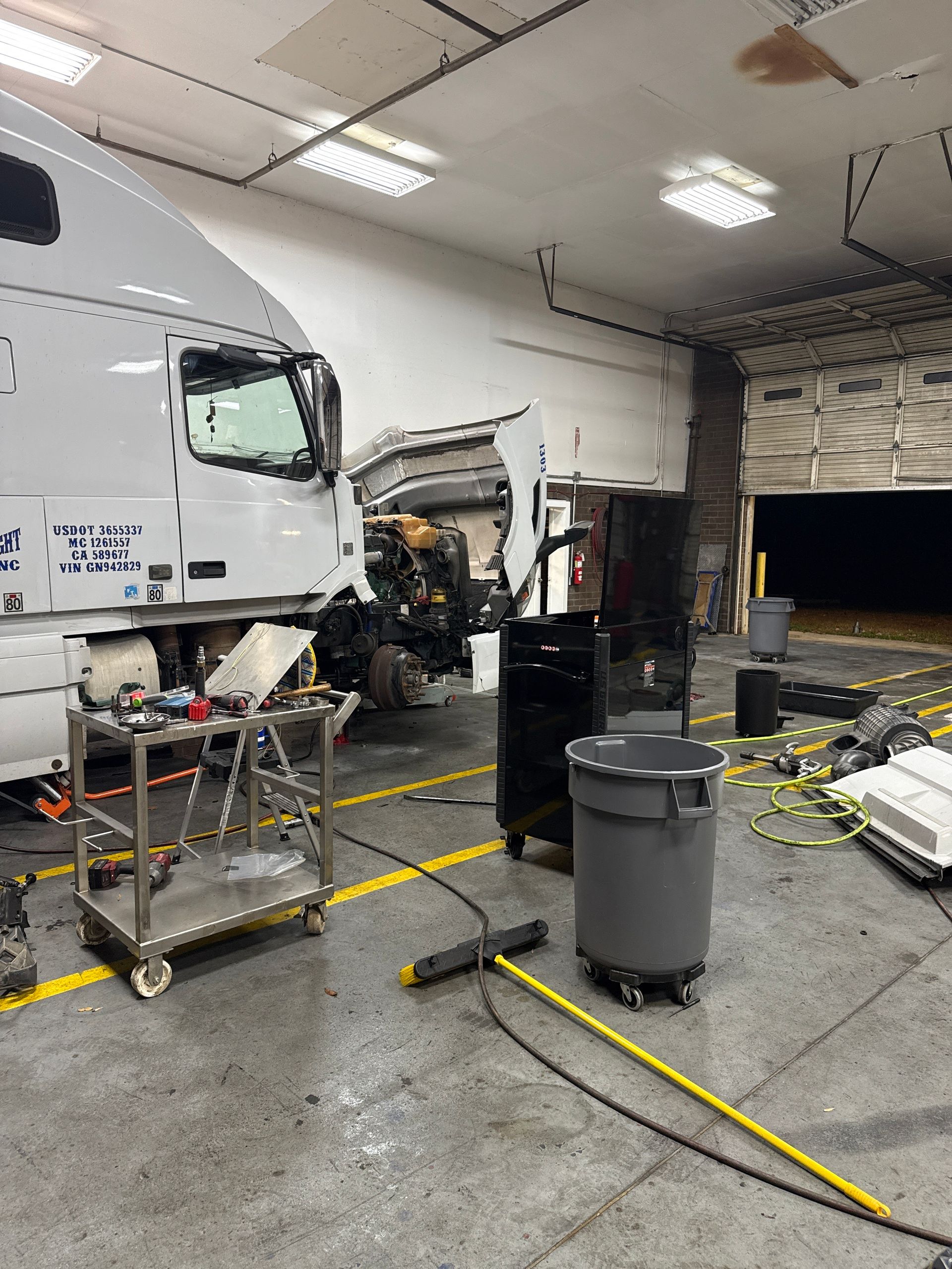 Truck repair shop with a white semi-truck, tools, and equipment on the garage floor