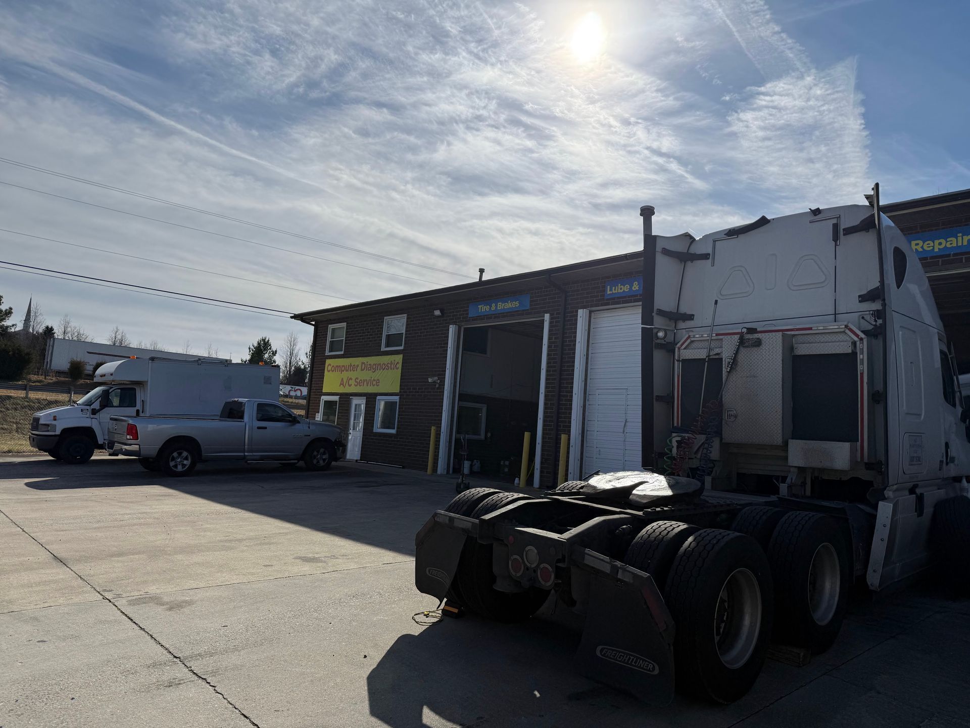 Semi truck with white trailer parked outside a warehouse on a sunny industrial lot.