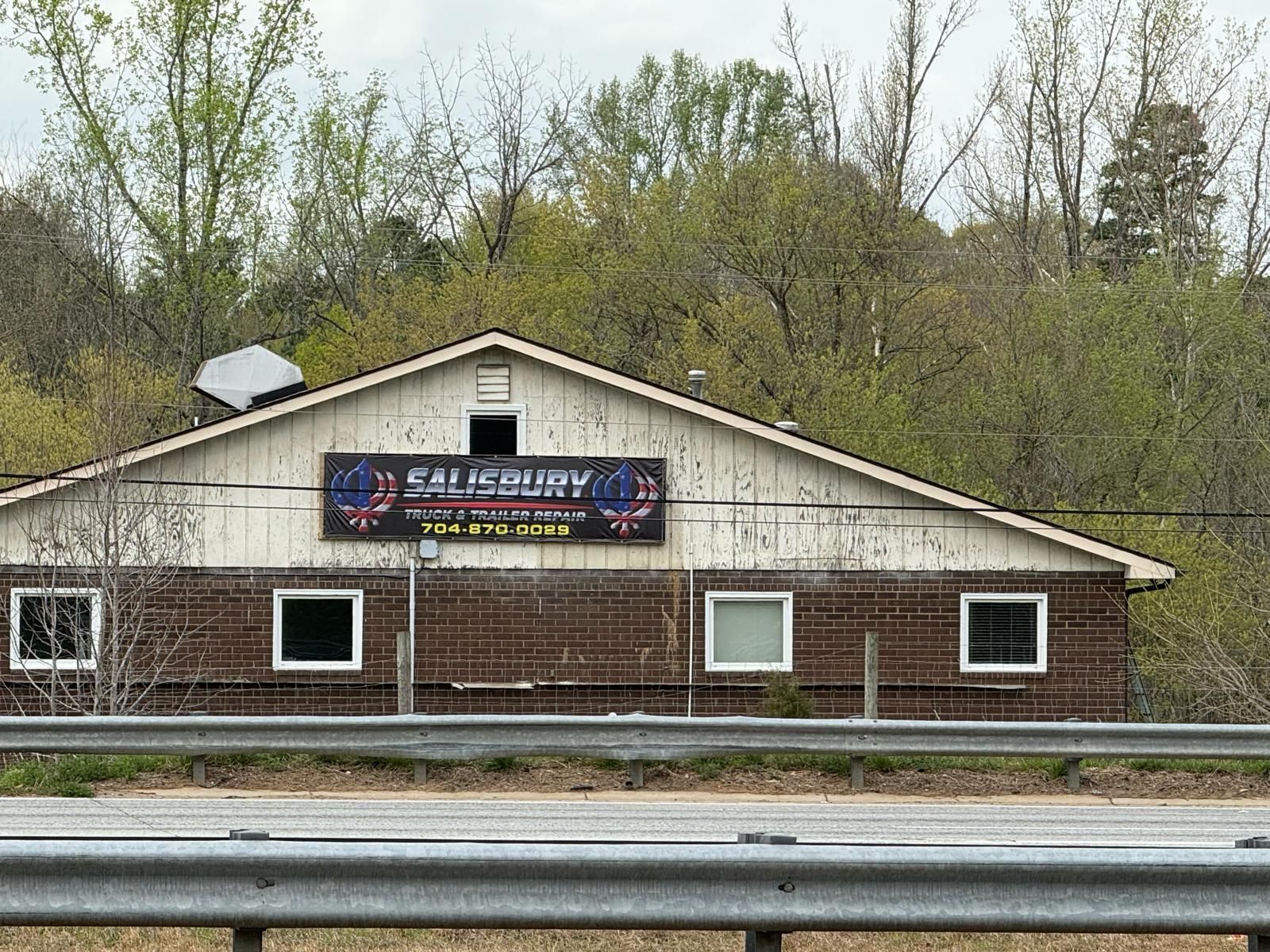 Small roadside building with a banner sign, white trim, and trees in the background