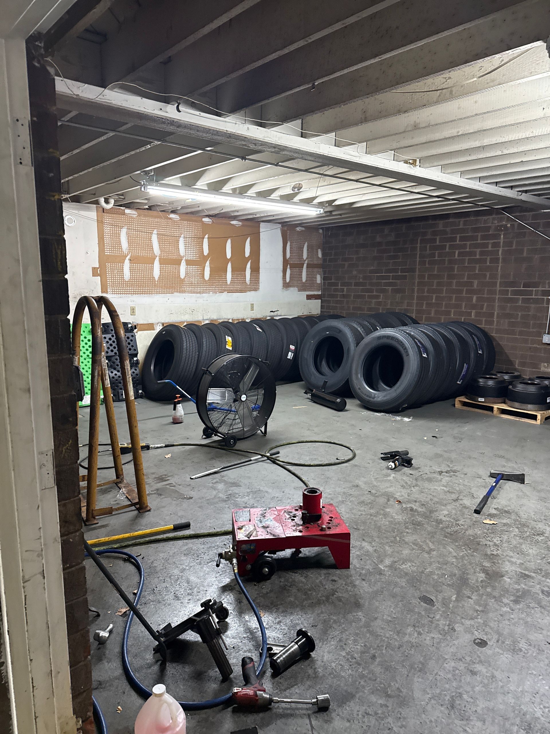 Tire repair shop interior with stacked tires, tools on the floor, and a brick wall under a metal roof
