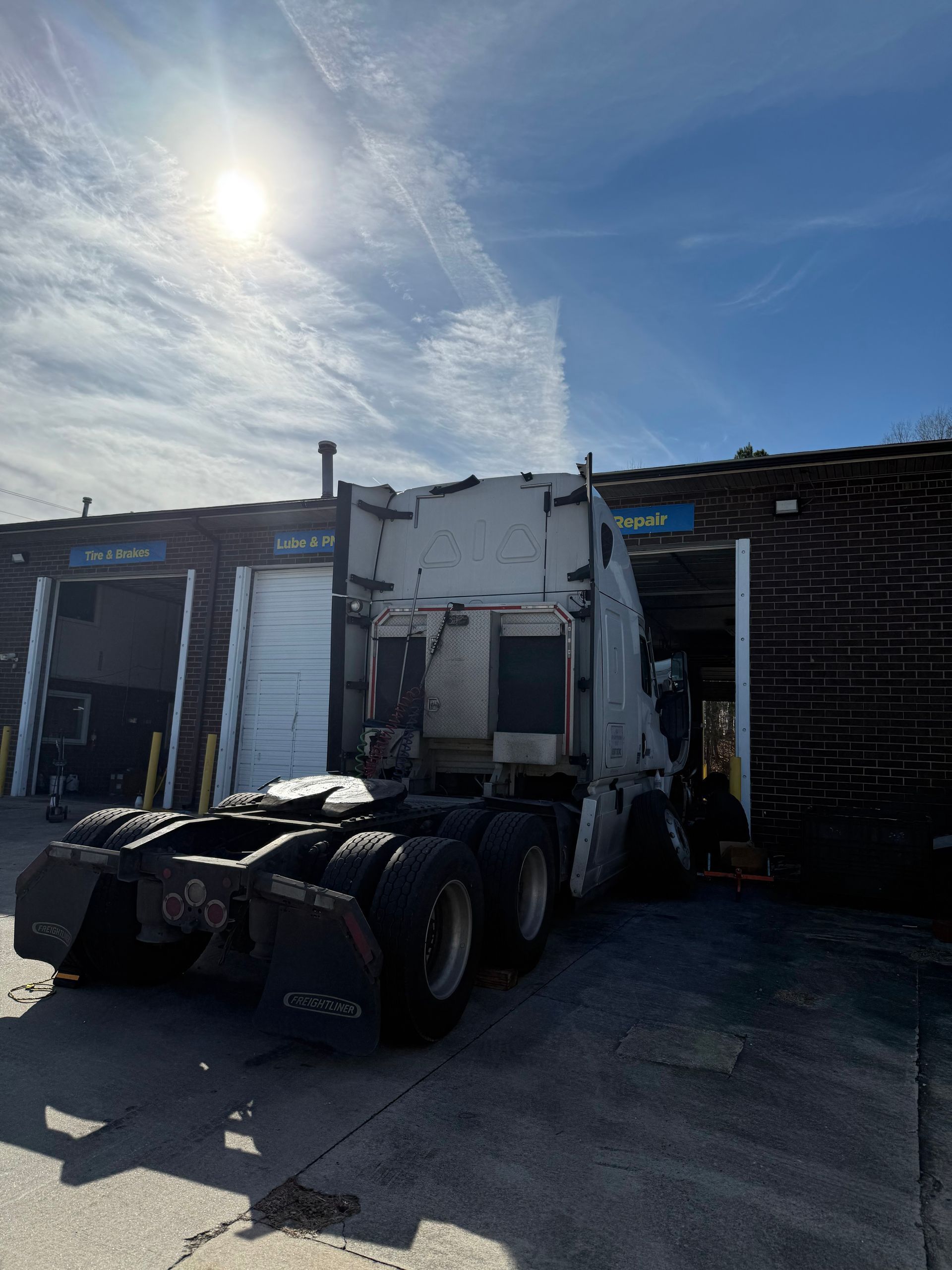 White semi-truck tractor parked beside an industrial building in bright sunlight