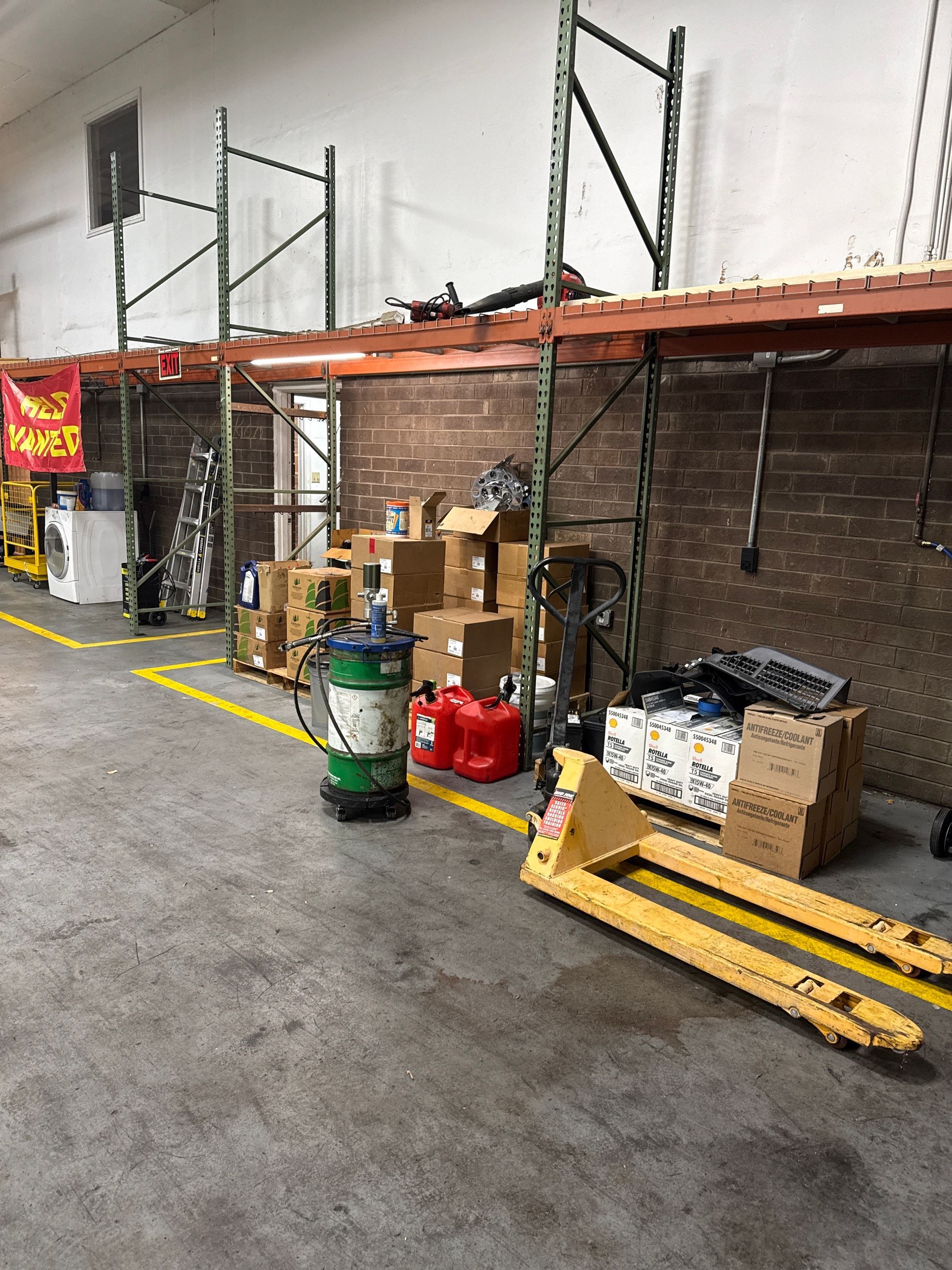 Warehouse aisle with shelving, stacked boxes, gas cylinders, and yellow pallet jacks on a concrete floor