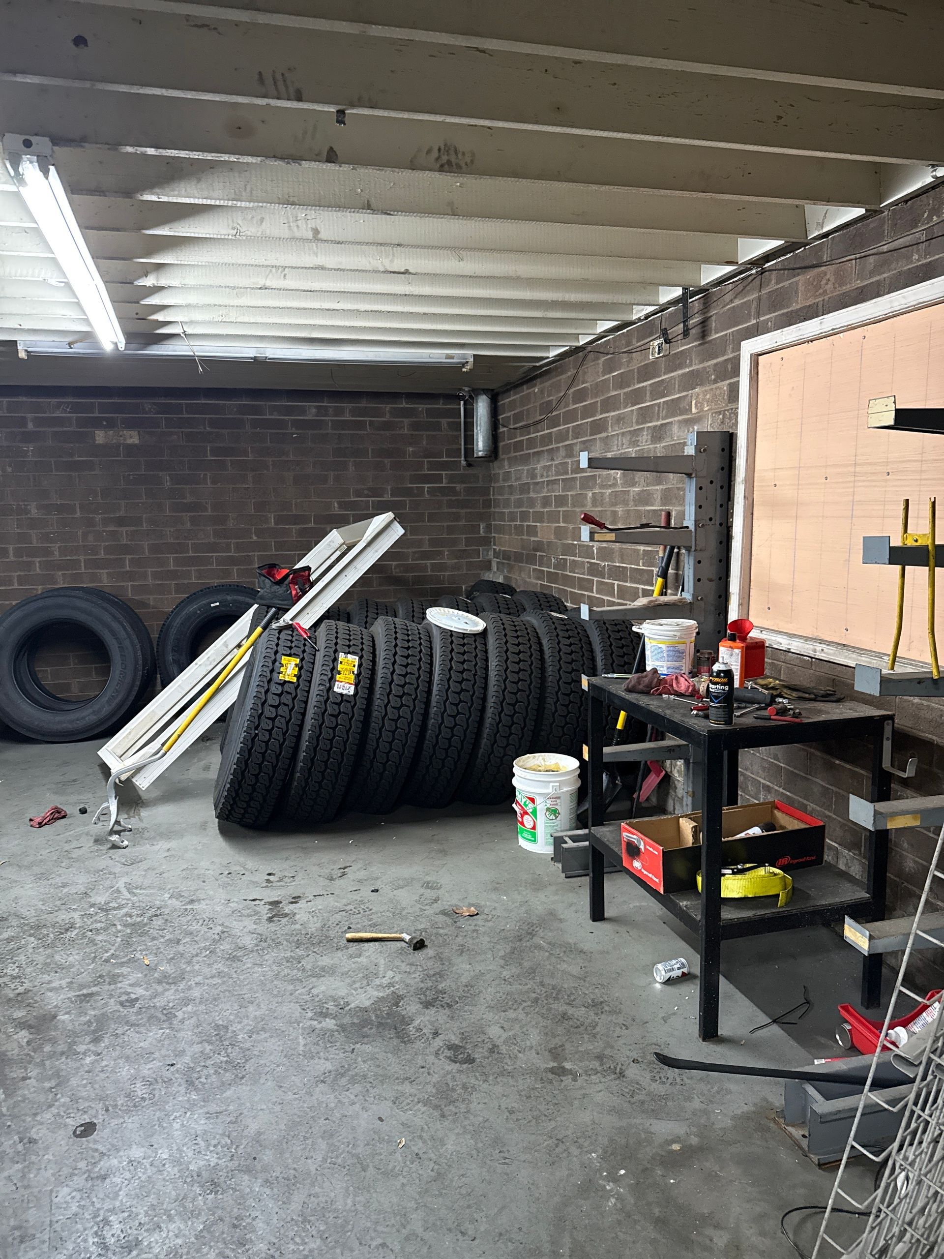 Garage with stacked tires, metal shelving, and tools beside brick walls under a covered roof.