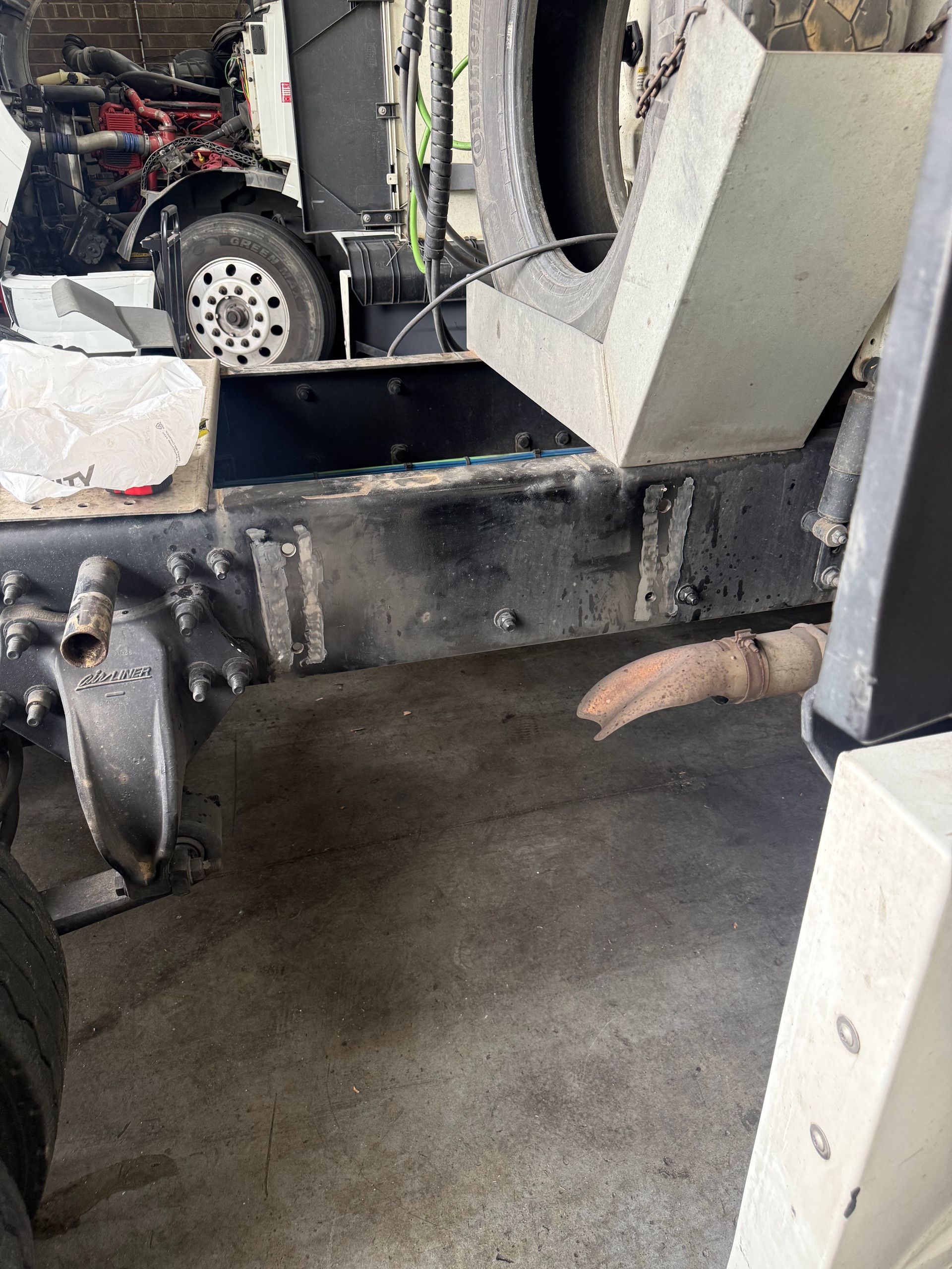 Indoor industrial machine with black metal frame, white hopper, and concrete floor, with a cable hanging below.