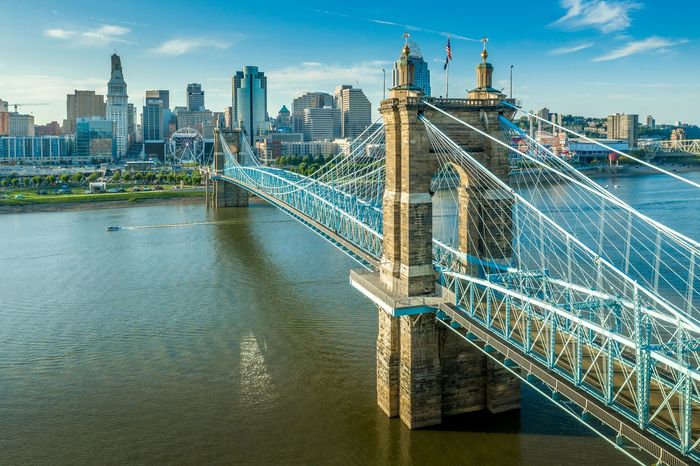 An aerial view of a bridge over a river with a city skyline in the background.