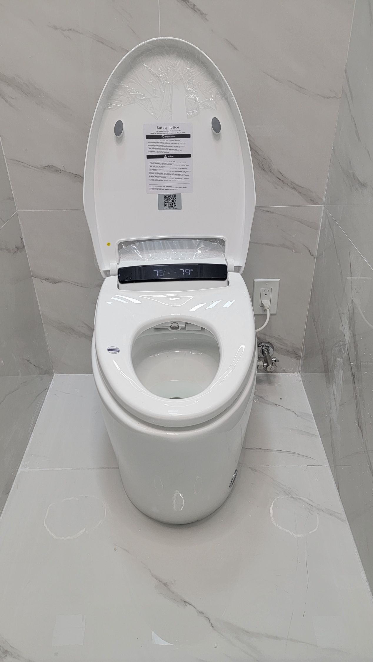 Modern white toilet with lid open against marble-look tiled wall