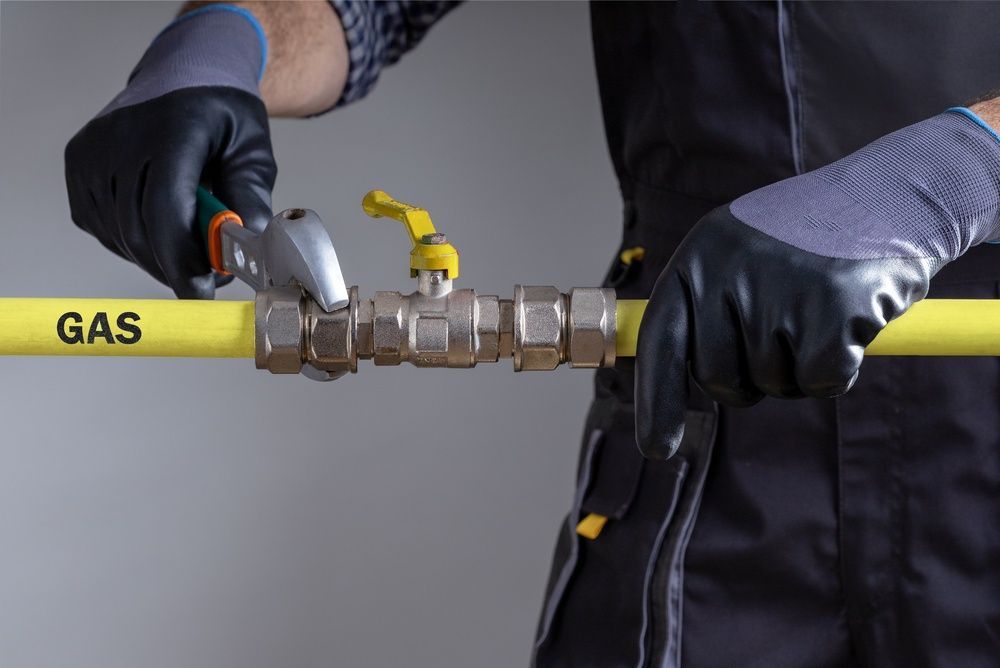 Gloved hands adjusting a yellow gas pipe valve with wrench and shutoff handle