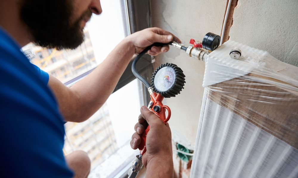 Technician using a pressure gauge to inspect a wrapped HVAC unit near a window
