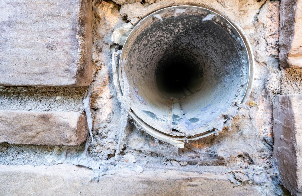 Close-up of a stone wall with a circular metal pipe opening and chipped plaster around it