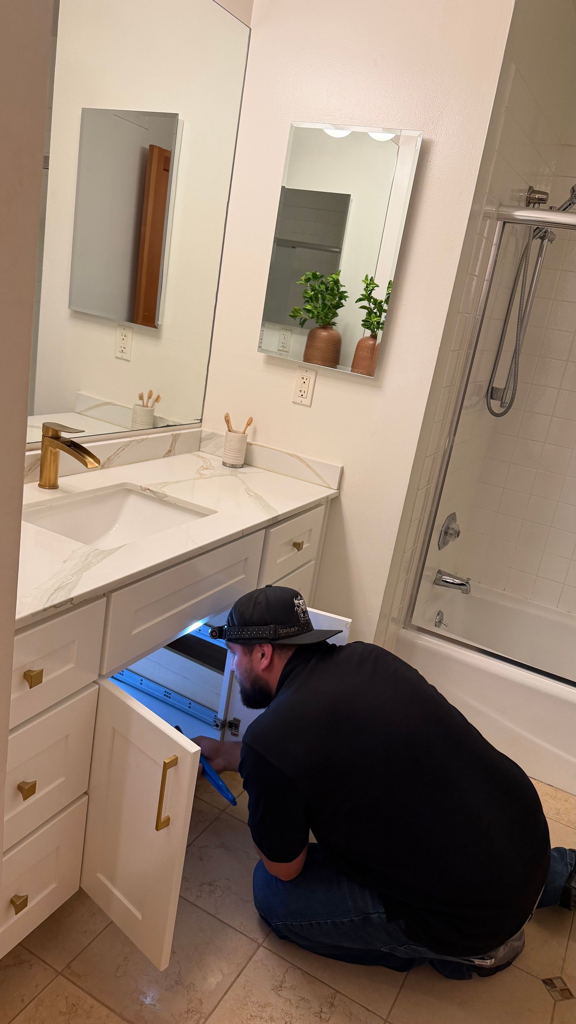 Gloved hands tightening a chrome sink drain pipe under a bathroom sink