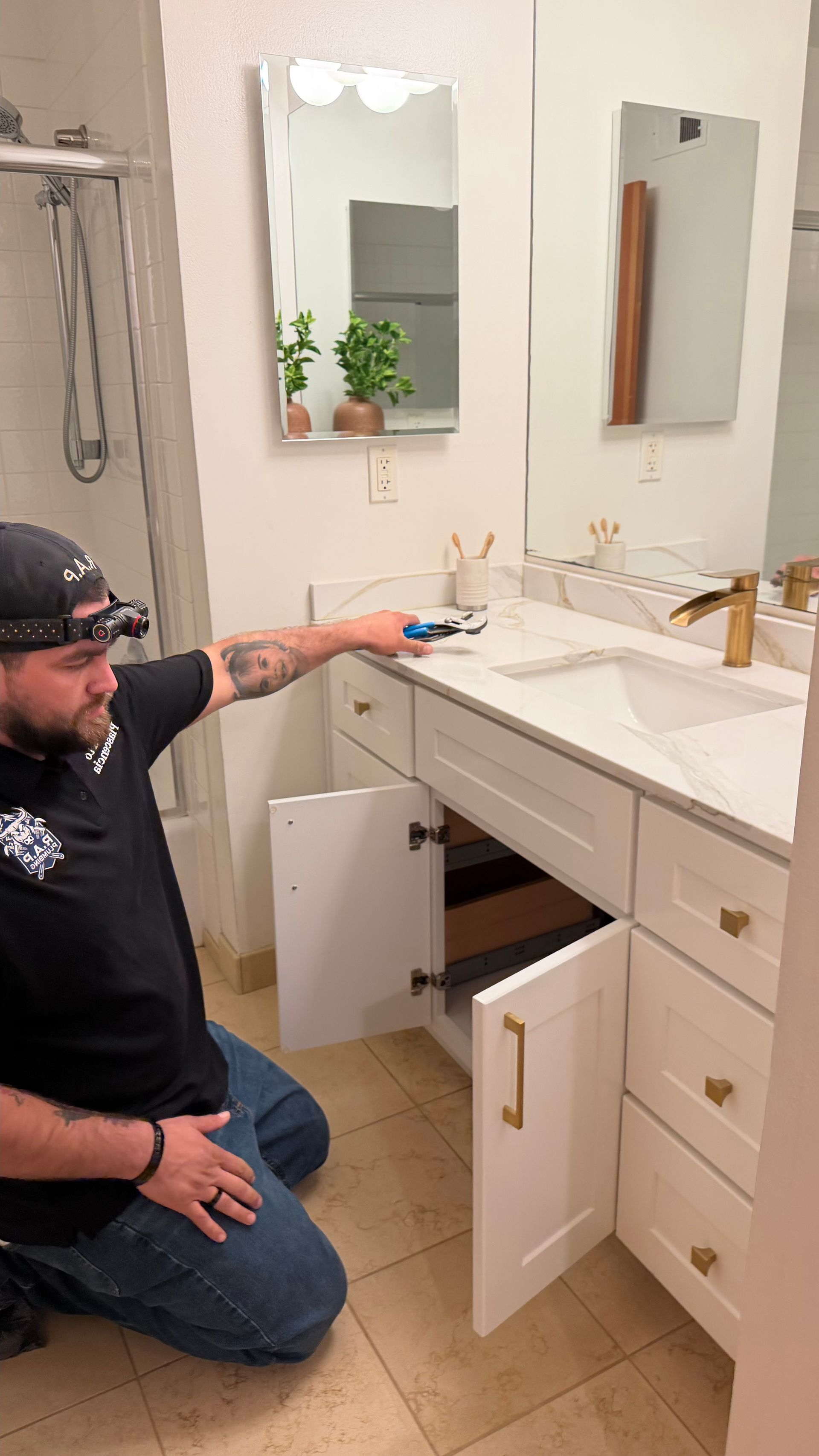 Plumber in blue overalls fixing pipes under a kitchen sink with tools on the floor