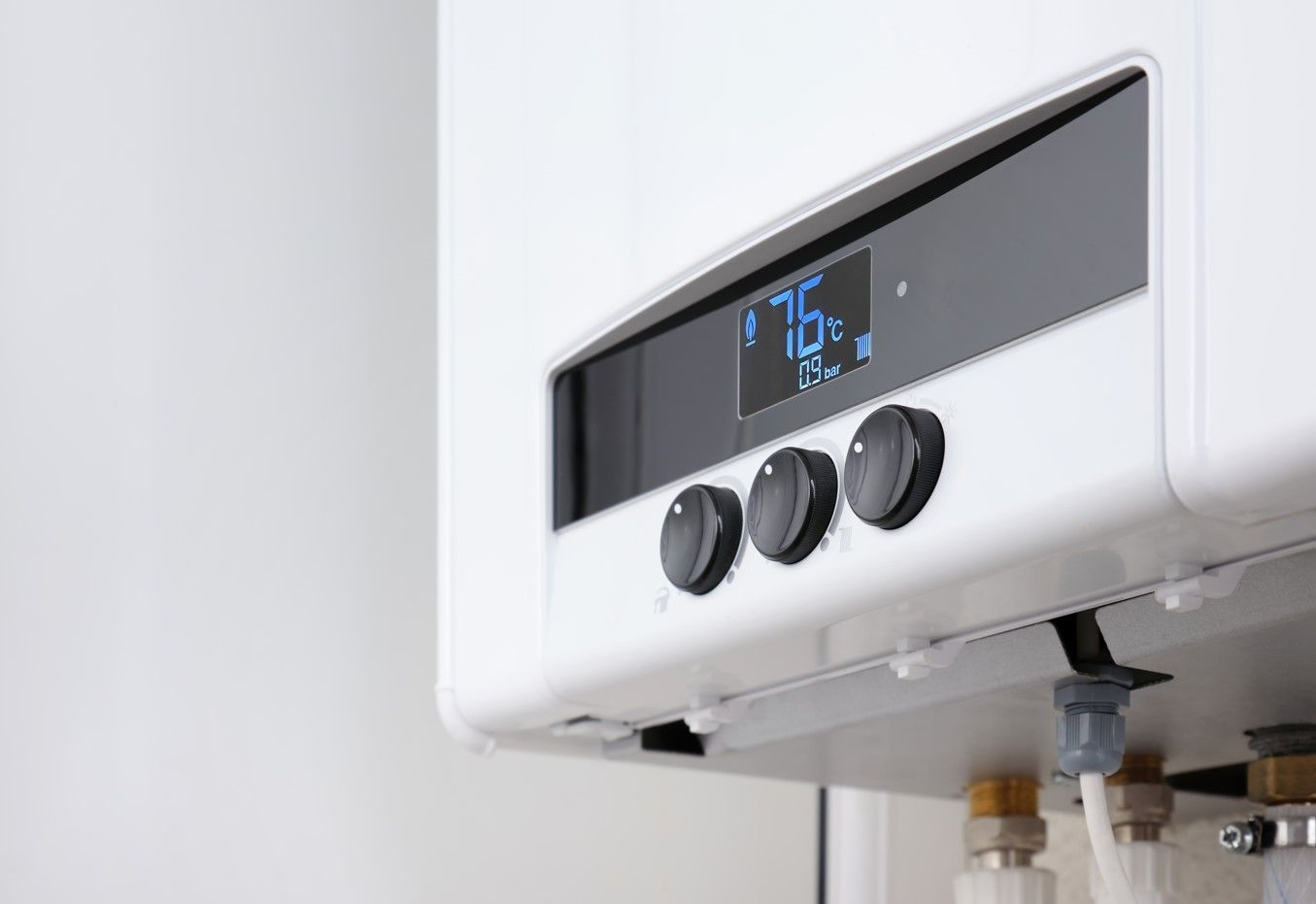 White wall-mounted water heater with digital display and three black control knobs above plumbing pipes