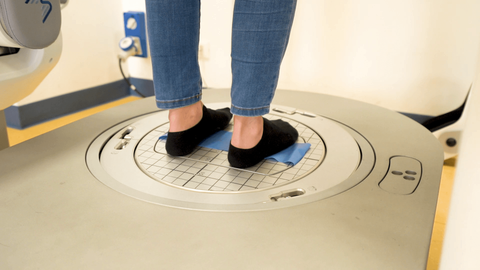 Persona in piedi su una piattaforma circolare per la misurazione del corpo, con calzini neri e jeans.