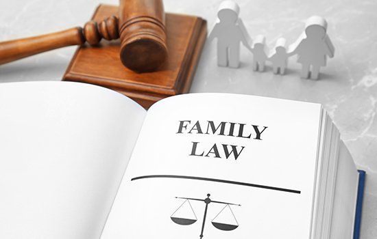 Family law book open with gavel, paper family figures, and scales icon on marble surface.