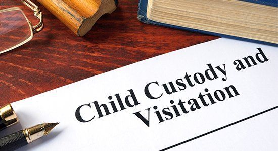 Child Custody and Visitation document with pen, eyeglasses, and book on a wooden desk.