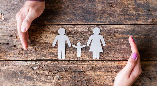 Hands cupping paper cutouts of a family on a wood surface.