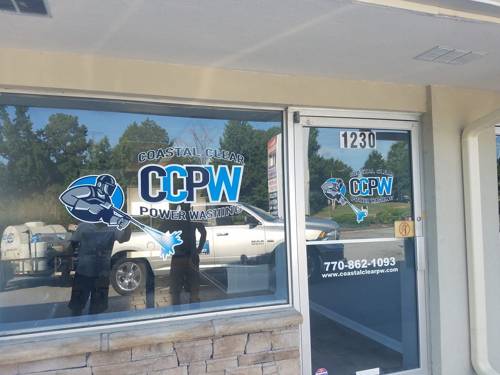 The front window and door of a storefront displaying the blue and white CCPW Powerwashing logo, phone number, and website.