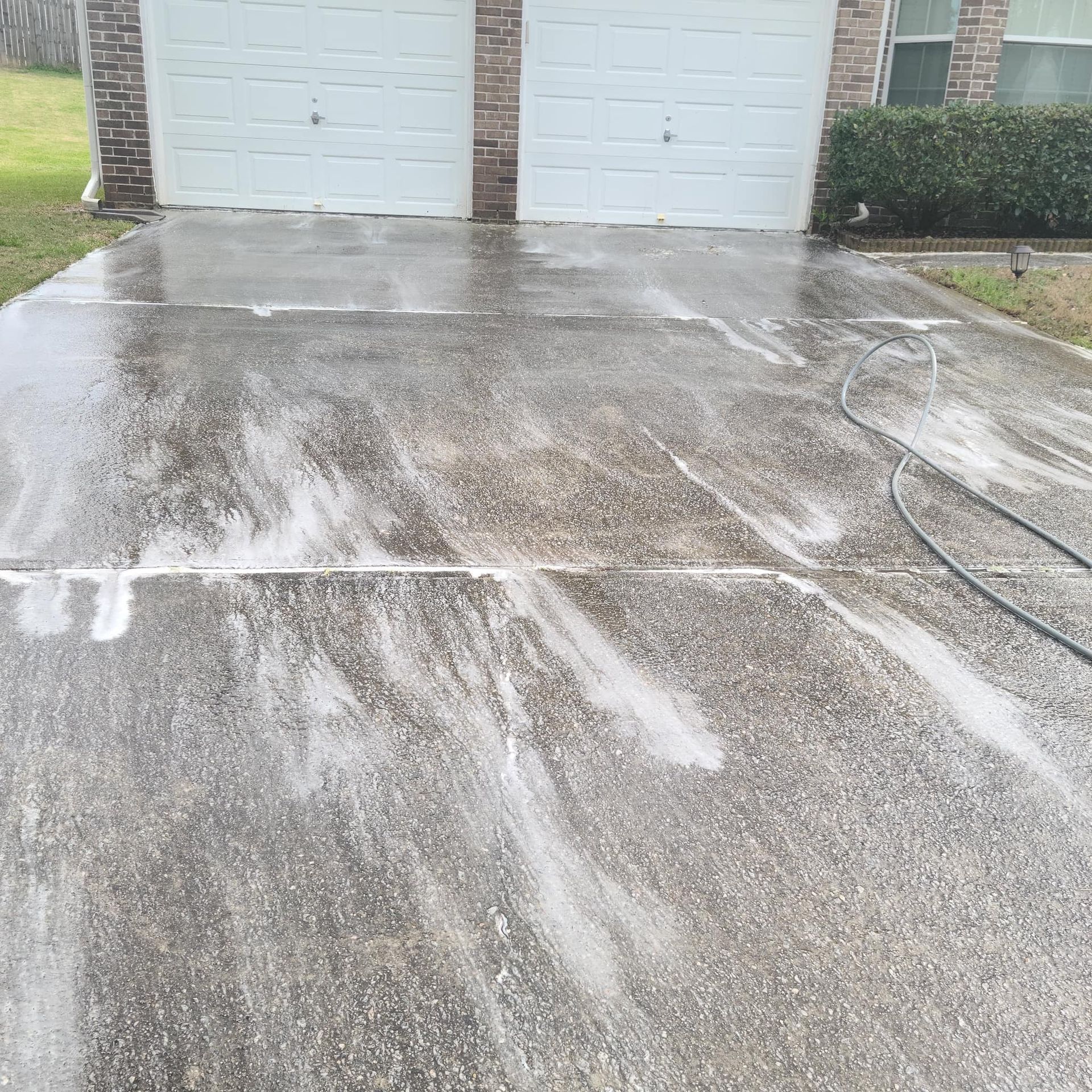 A wet, soapy driveway being power-washed in front of a two-car garage.