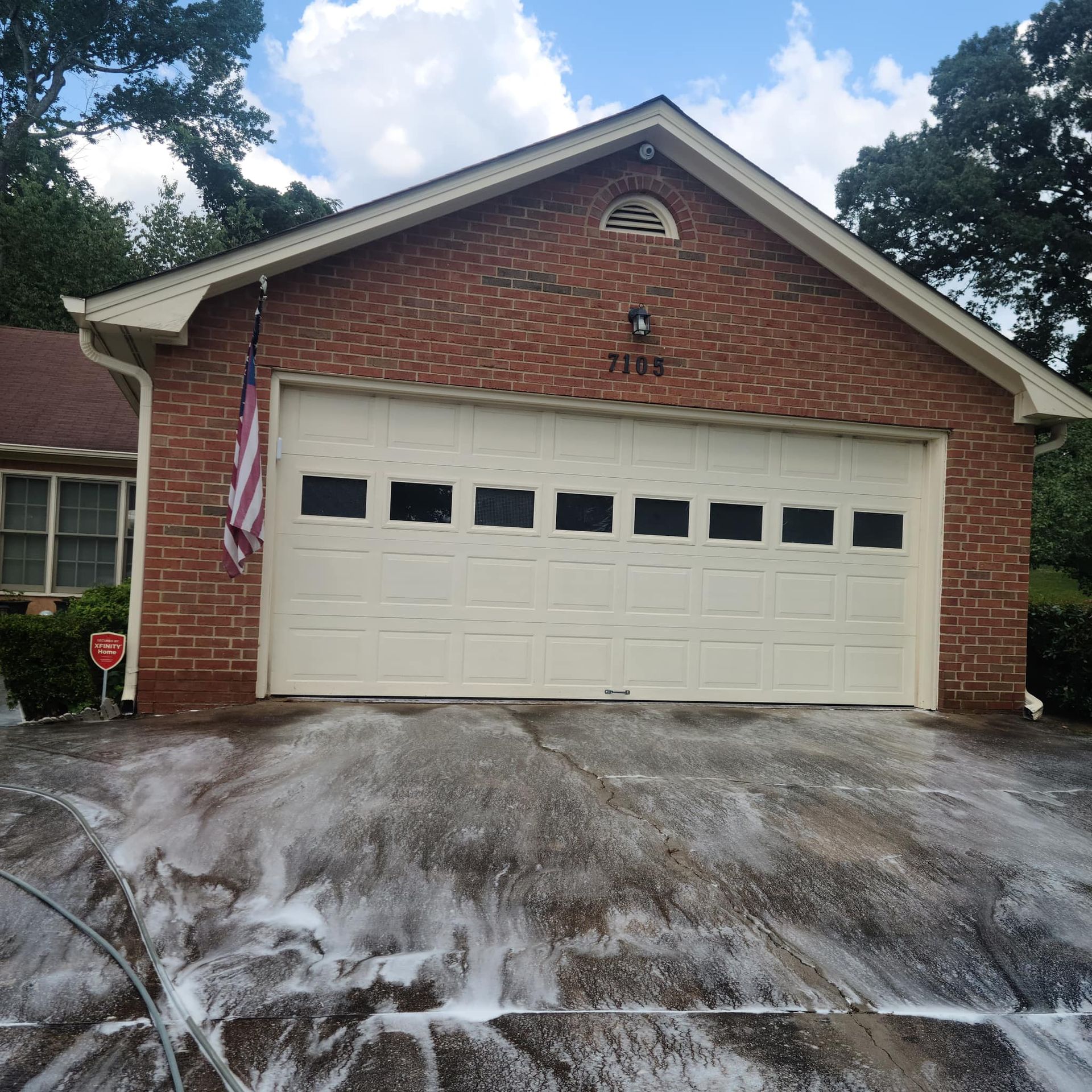 A brick house with a cream-colored garage door and soapy water cleaning solution covering the concrete driveway.