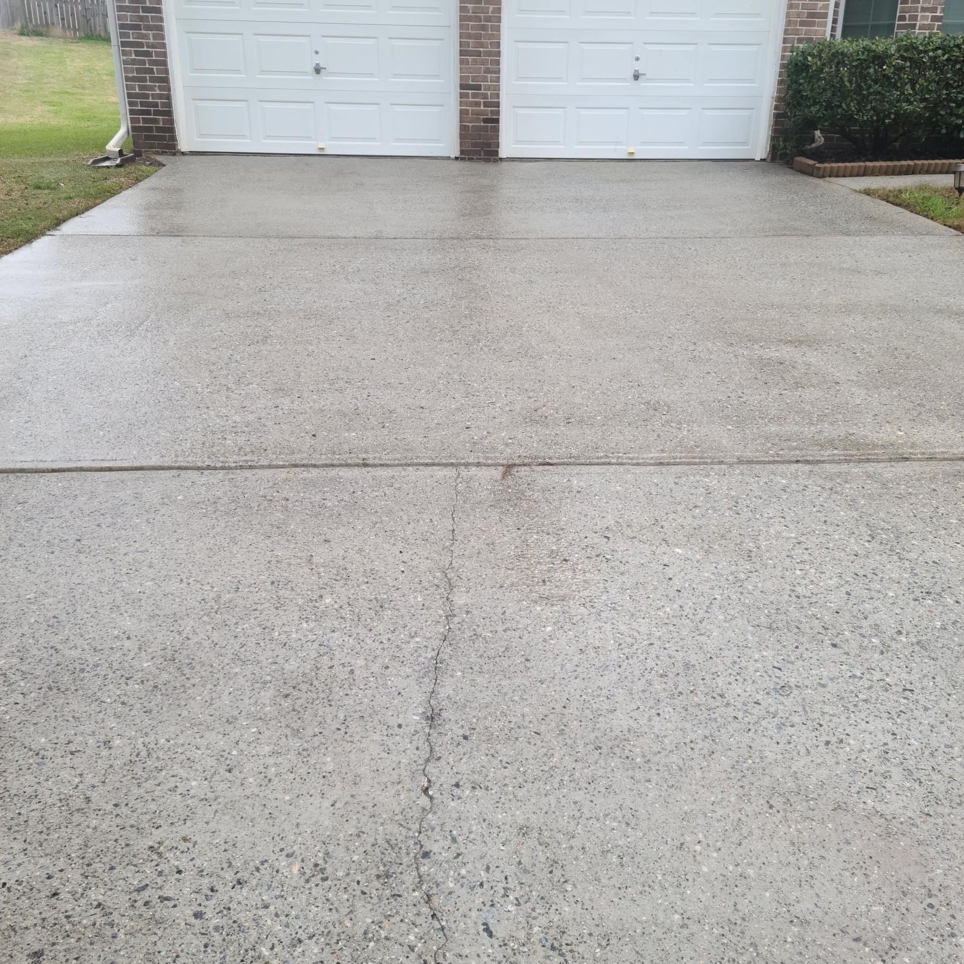 A gray concrete driveway leads to a two-car garage with white doors, showing a visible crack in the foreground.