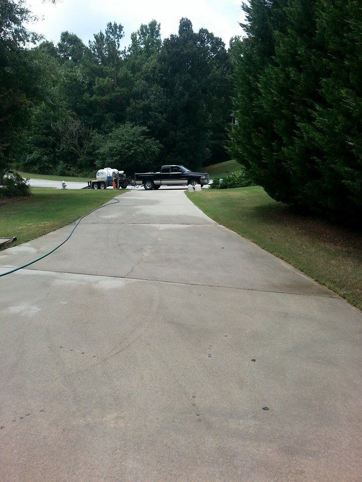 A black pickup truck with a white trailer parked on a concrete driveway surrounded by trees and a green lawn.