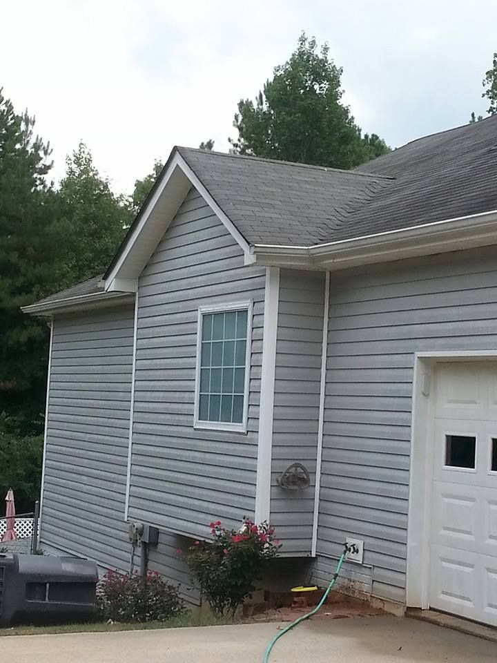 A gray vinyl-sided house exterior with a window, a white garage door, and trees in the background.