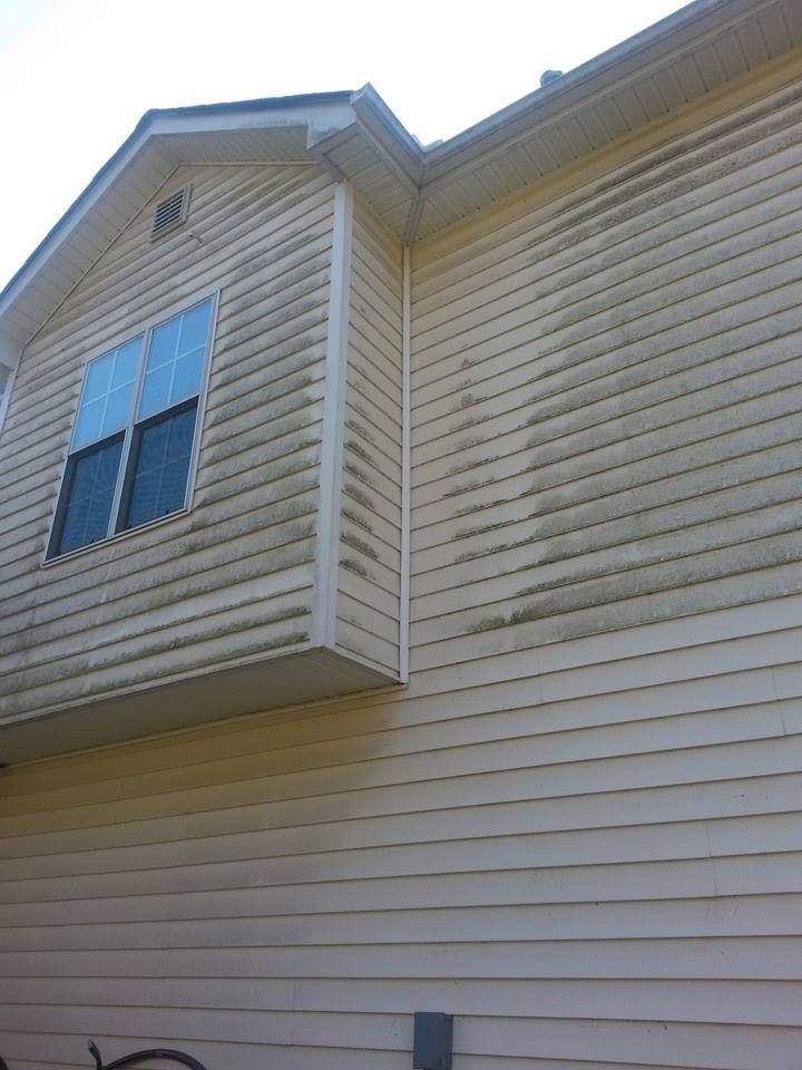 Exterior side of a house with light yellow siding featuring noticeable streaks of dark algae or dirt buildup.