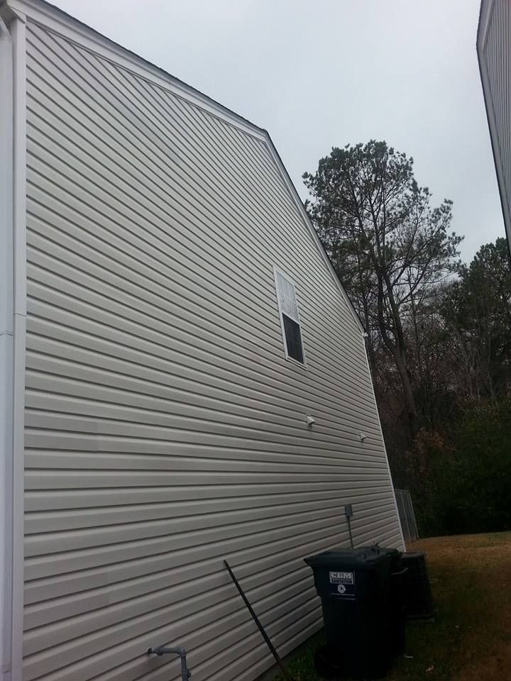 The side of a two-story beige house with horizontal vinyl siding and a single window, next to a black trash bin.