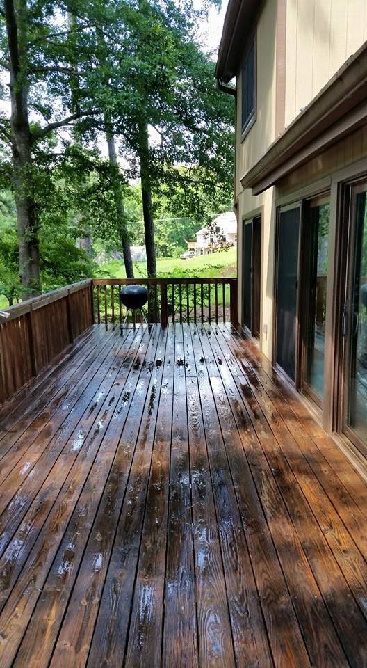 A wet, wooden deck overlooking a tree-filled backyard with a house exterior and sliding glass doors to the right.