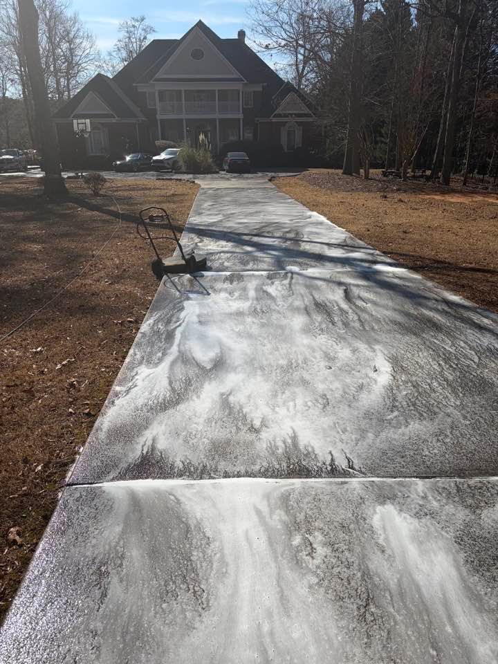 A long driveway covered in white cleaning foam leading to a two-story house with a lawn and trees in the background.