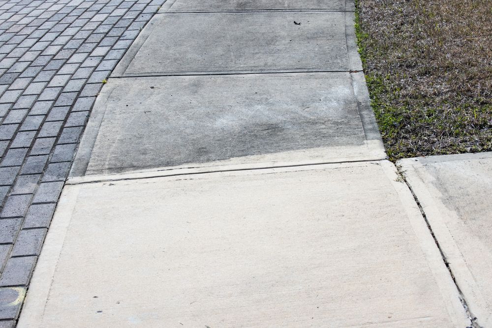 A sidewalk transition with a light concrete slab bordering darker, weathered concrete sections alongside cobblestones.
