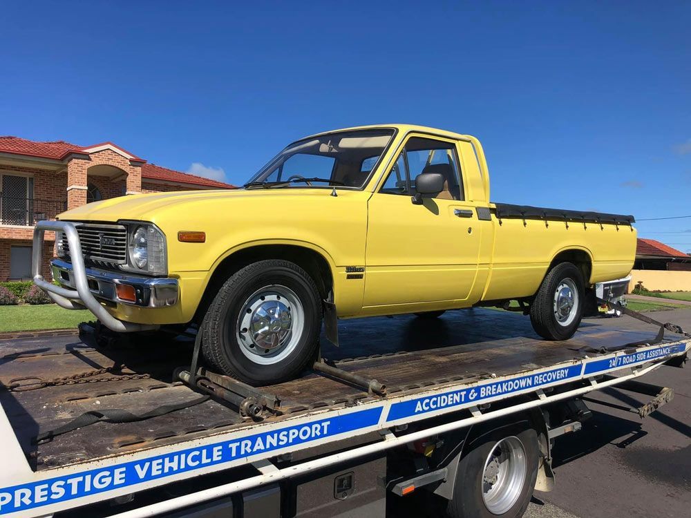 Yellow Toyota Pickup Truck On A Flatbed Tow Truck, Under A Blue Sky