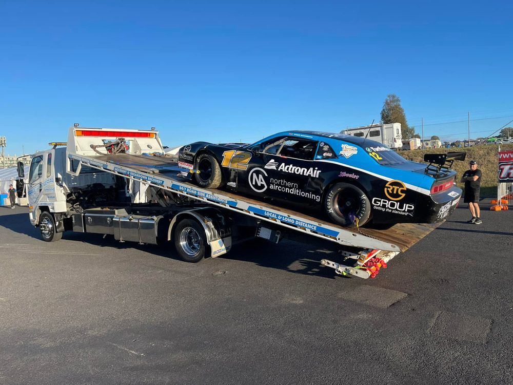 Towing the Black Racing Car With Action Air Stickers — Trade & General Towing in Sandgate, NSW